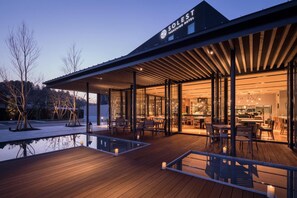 A modern hotel with a covered outdoor area featuring wooden flooring and glass walls. - Solest Takachiho Hotel (Takachiho)