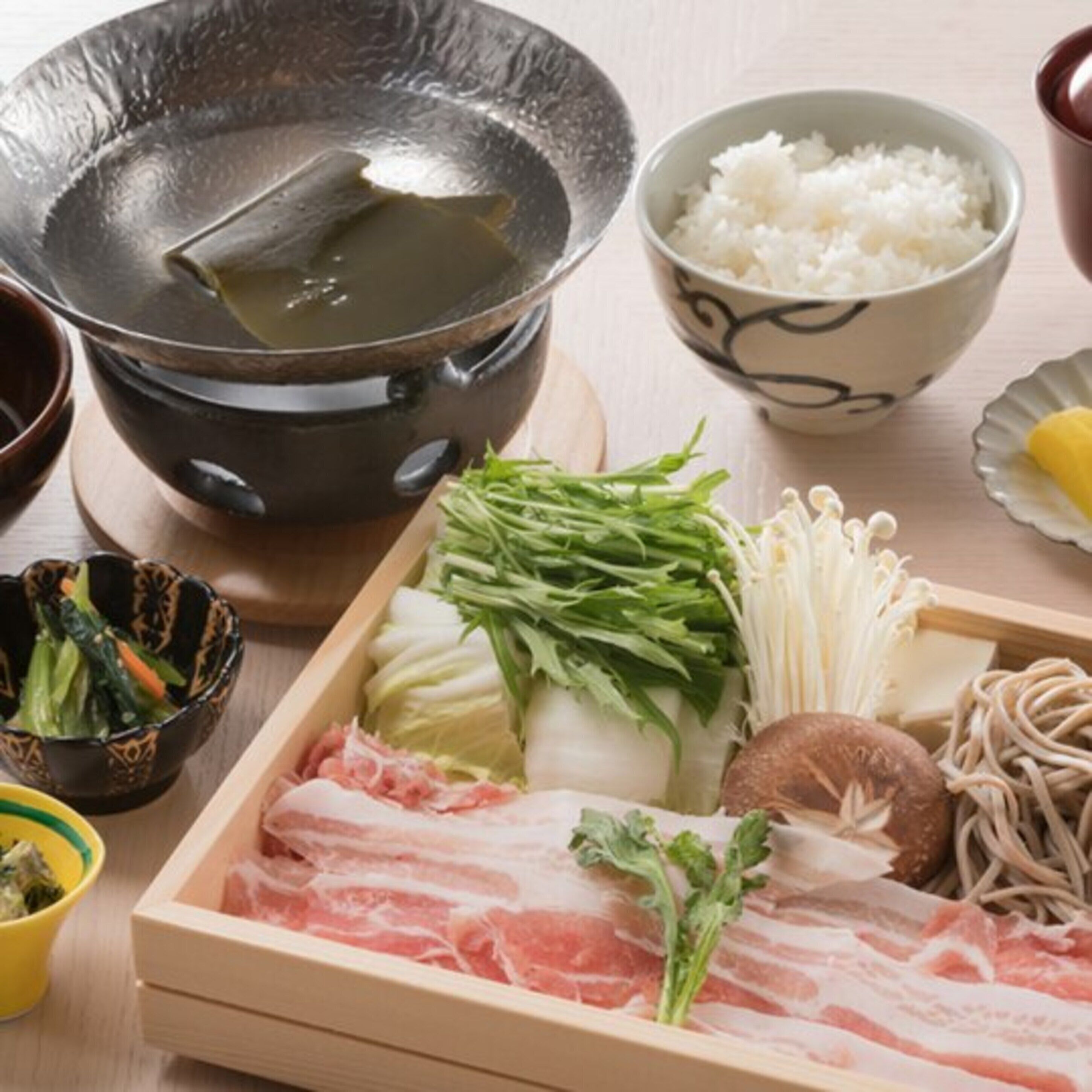 A traditional Japanese meal setup with a hot pot, rice, various vegetables, and raw meat.