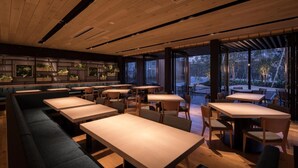 Un restaurant doté de longues tables en bois et de bancs rembourrés, de grandes fenêtres offrant une vue sur l’extérieur et d’un aménagement intérieur moderne.