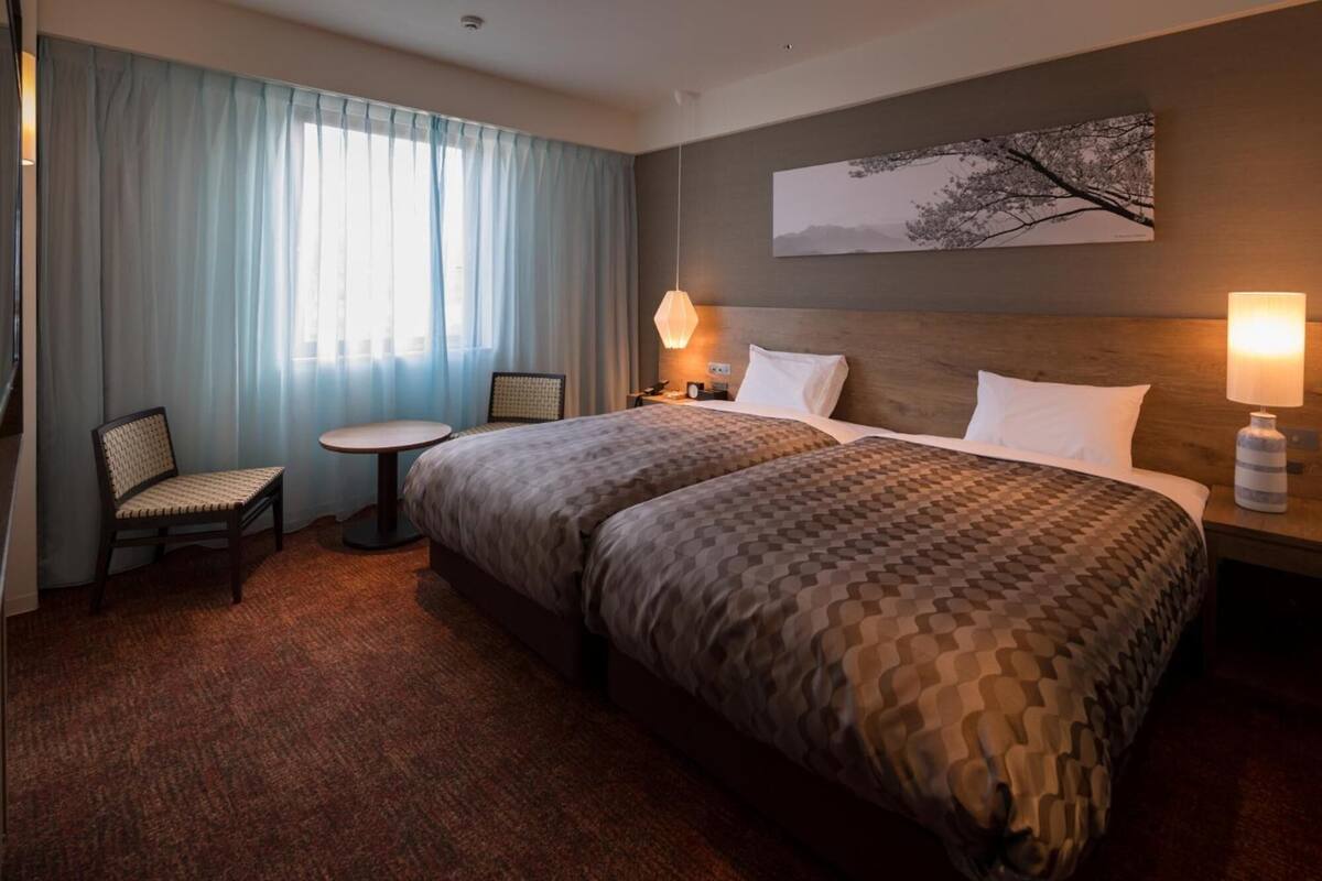Habitación de hotel con una cama grande, una mesita pequeña, una silla y un cuadro en la pared.