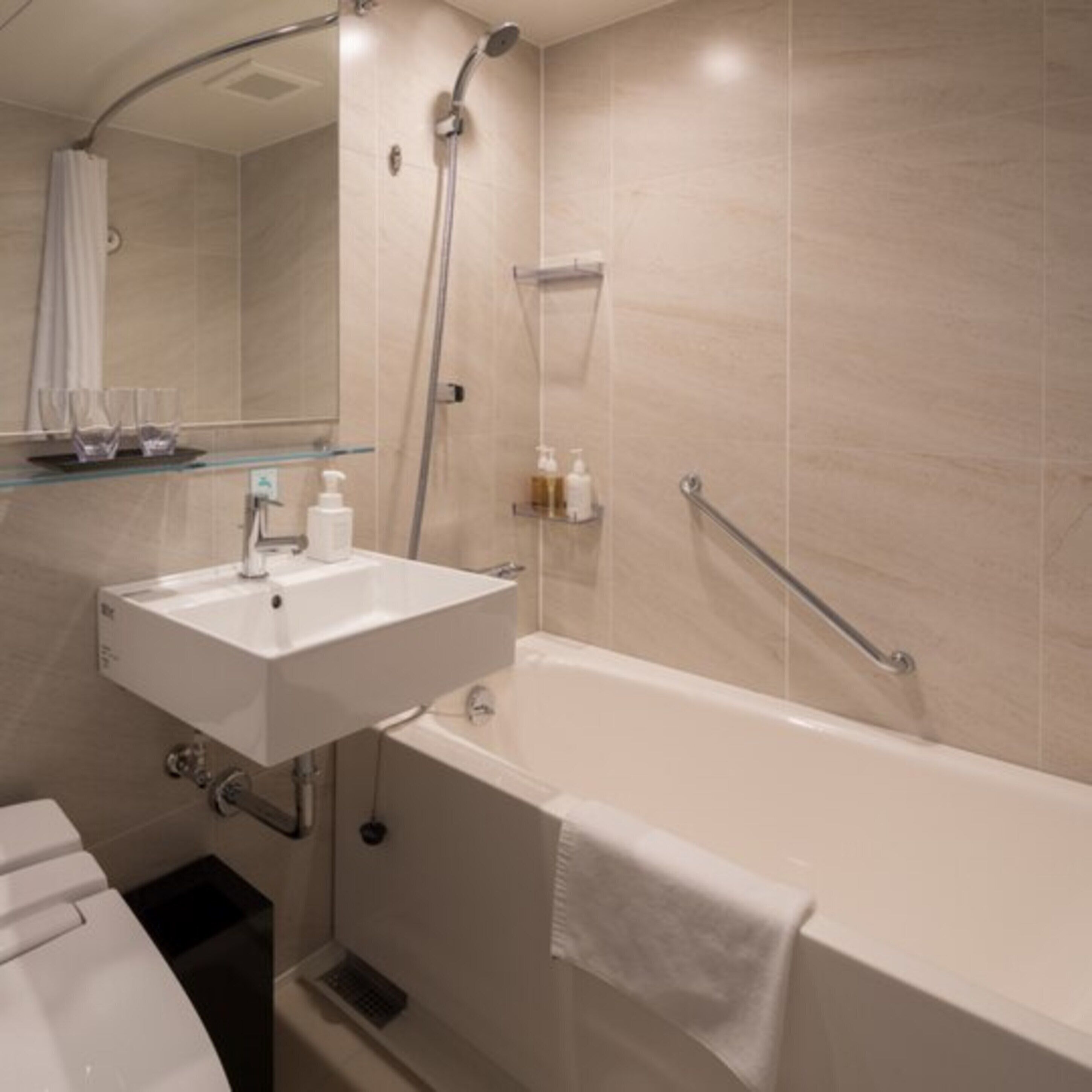 A modern bathroom with a white sink, mirror, and bathtub. There is a showerhead and a glass shelf with toiletries.