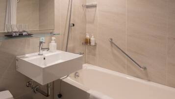 A modern bathroom with a white sink, mirror, and bathtub. There is a showerhead and a glass shelf with toiletries.