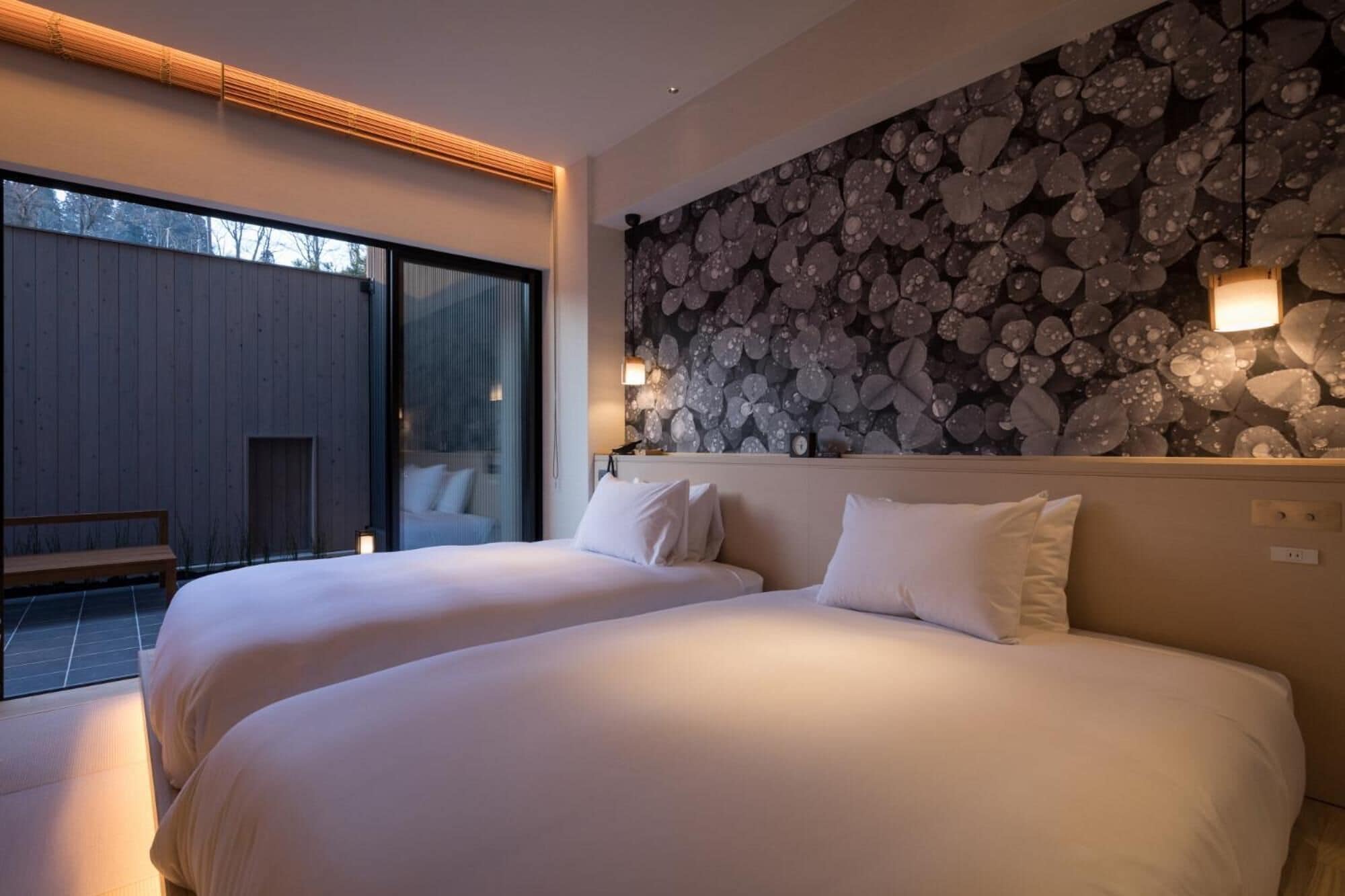 A bedroom with two beds, a wooden wall, and a view of the outside.