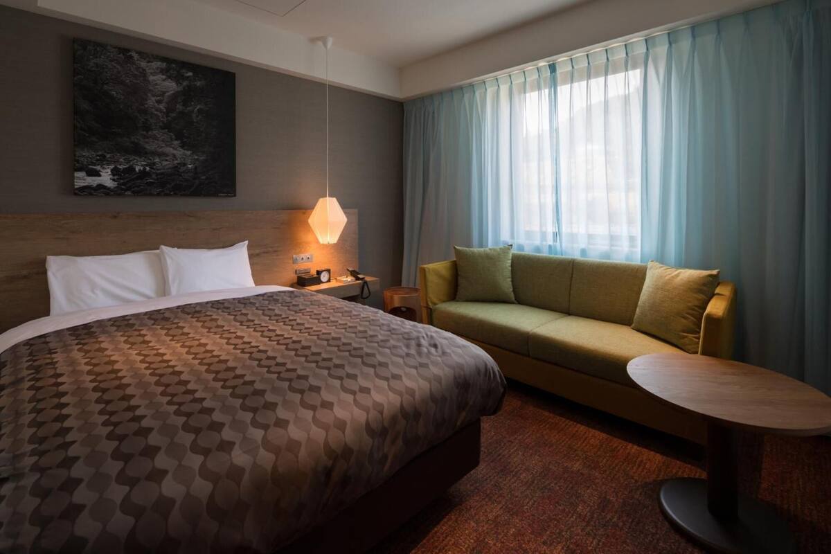 Habitación de hotel con una cama grande, un sofá, una mesita redonda y un cuadro en la pared.