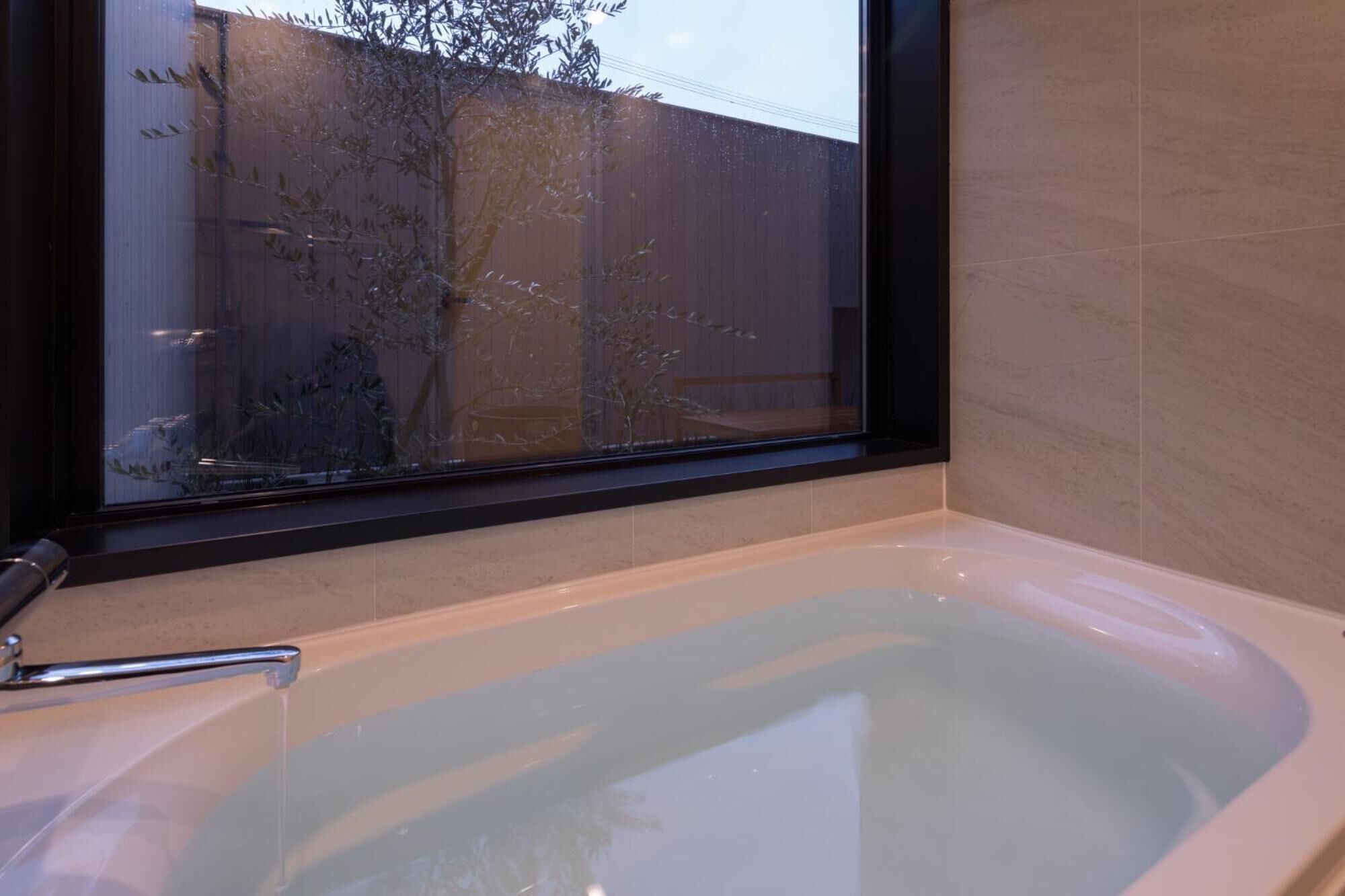 A bathroom with a bathtub, a window, and a view of a fence and trees outside.