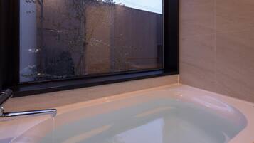 A bathroom with a bathtub, a window, and a view of a fence and trees outside.