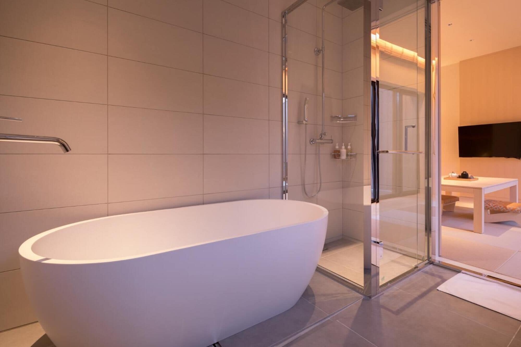 Ein modernes Badezimmer mit einer freistehenden Badewanne, einer Duschkabine aus Glas und einem sichtbaren Waschbeckenbereich.