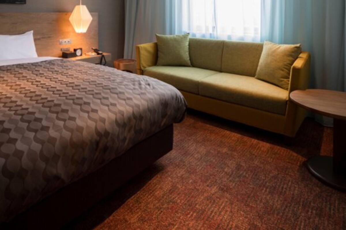 Una habitación de hotel con una cama grande, un sofá, una mesita y una ventana con cortinas.