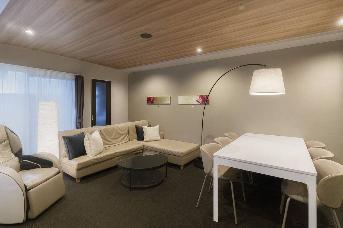 A modern hotel room with a sofa, a round coffee table, a dining table with chairs, and a floor lamp.