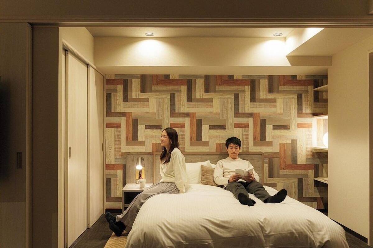A hotel room with a bed, a nightstand with a lamp, and a wall with a geometric pattern.
