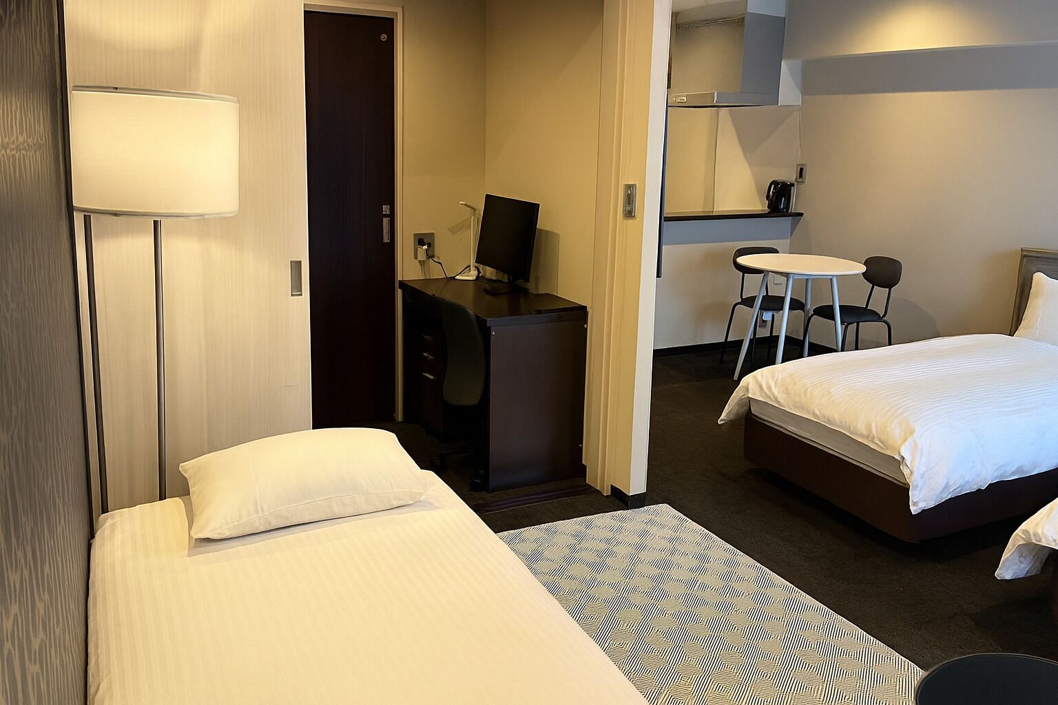 Une chambre d’hôtel avec deux lits, un bureau, une chaise, une petite table et un téléviseur.