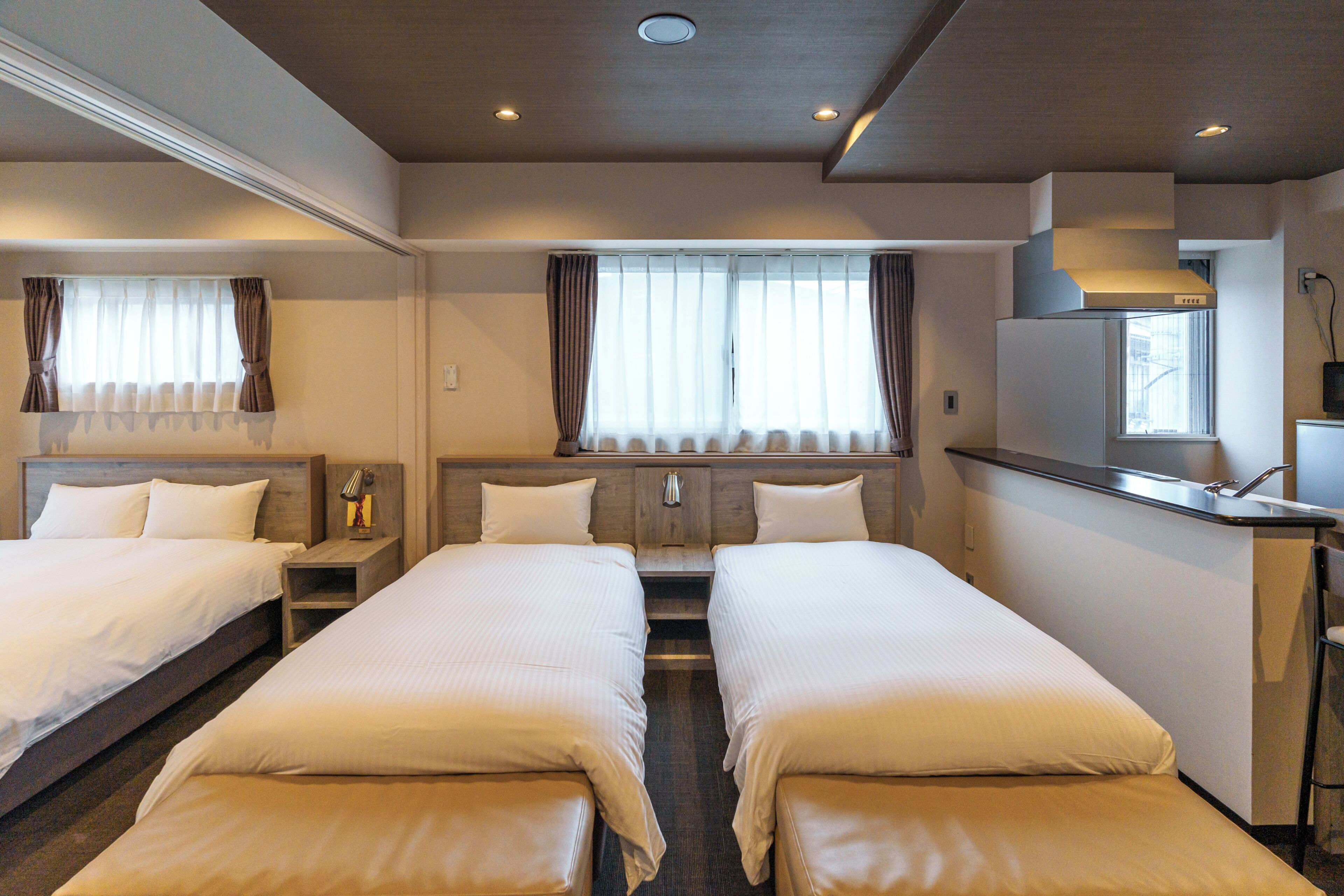 A hotel room with two beds, a small desk, and a window with curtains.
