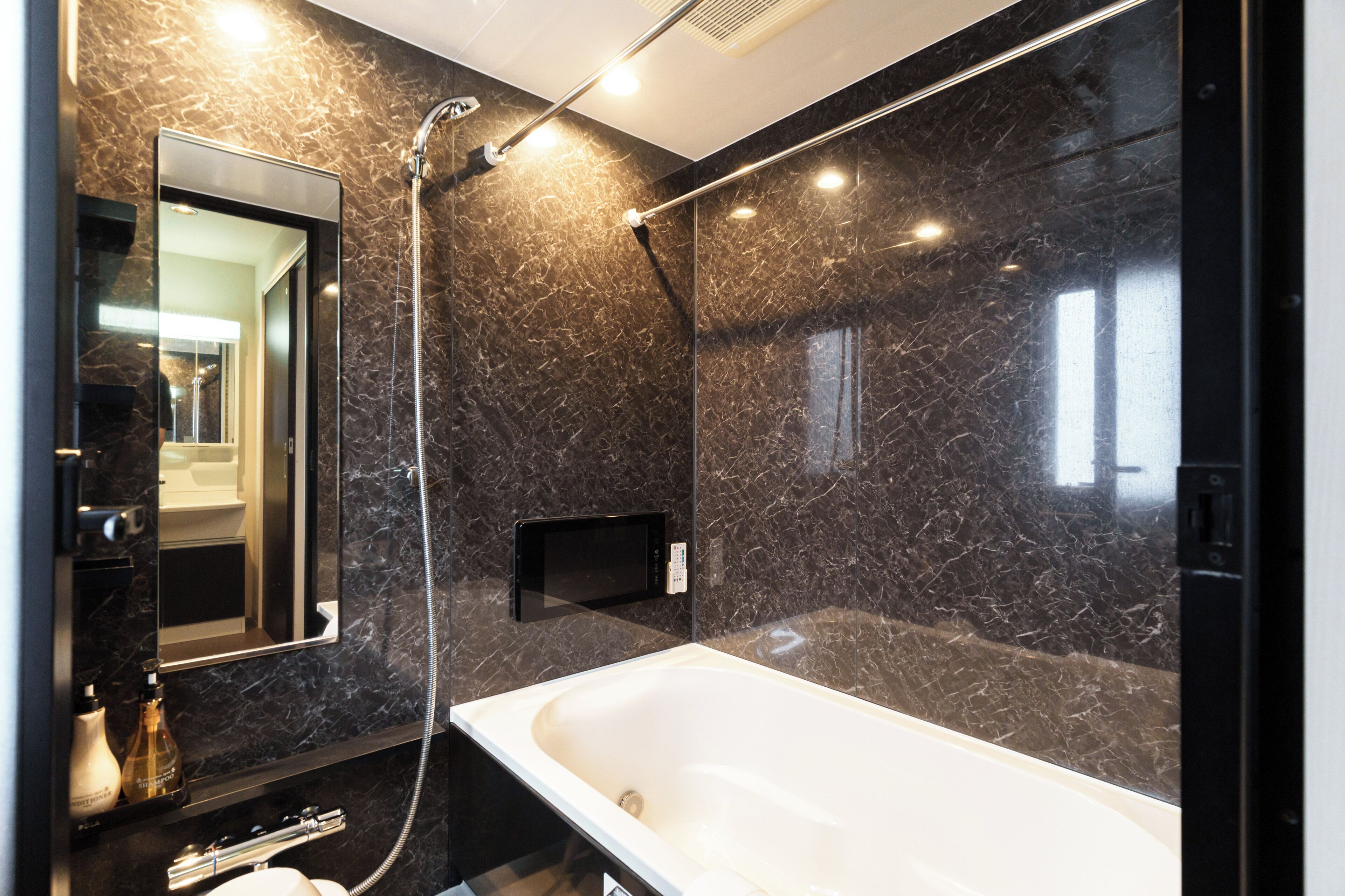 A modern bathroom with a large bathtub, a handheld showerhead, and a wall-mounted TV.