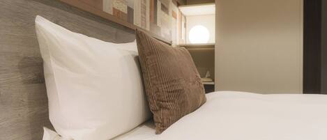 A neatly made bed with white and brown pillows, a wooden headboard, and a wall with a patterned design.