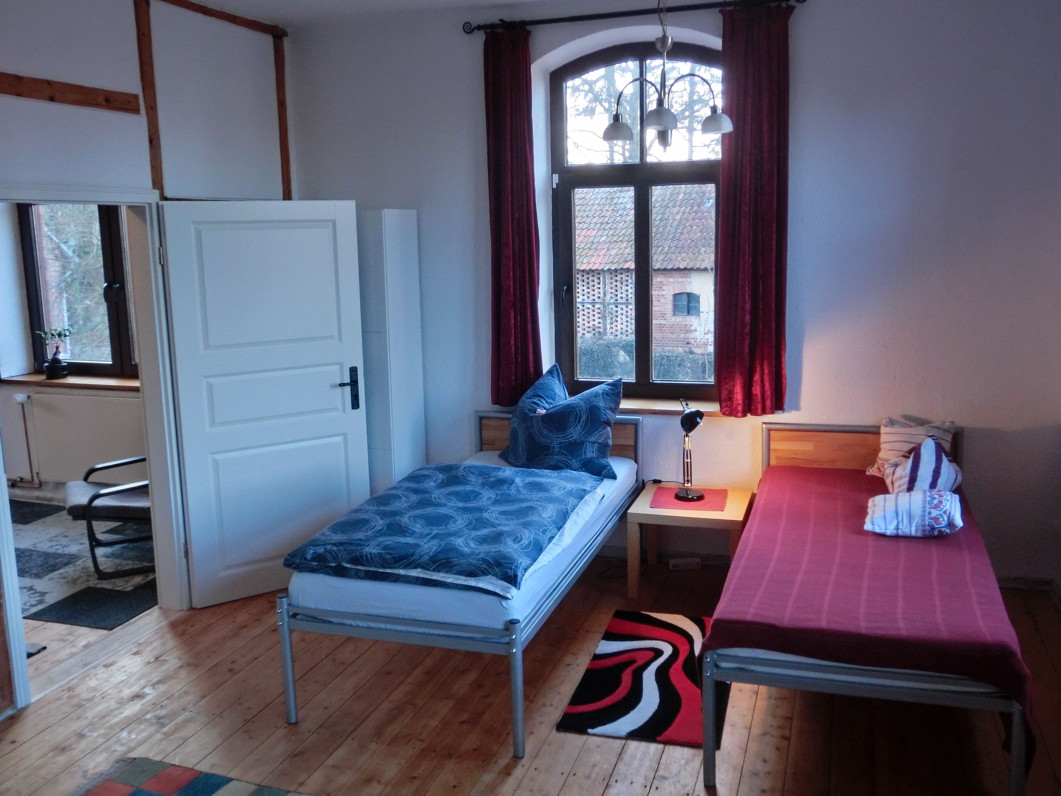 A room with a bed, a desk, a chair, a window with curtains, and a radiator.