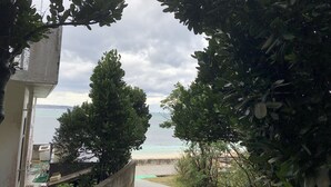 A pathway leading to a beach with a view of the sea, surrounded by greenery and a building on the left. - Mannnaya- (Motobu)