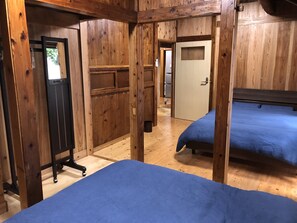 A wooden room with two beds, a mirror, and a door leading to another room.