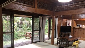 A traditional Japanese-style room with tatami flooring, a television, a wooden desk, and a view of a garden through large sliding doors. - Mannnaya- (Motobu)
