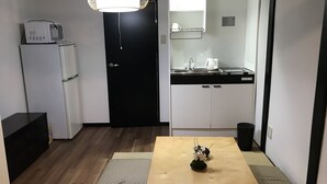 Kompakti keittiö, jossa on mikroaaltouuni, pesuallas ja vedenkeitin. Ruokapöytä maljakolla on sijoitettu huoneen keskelle.