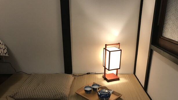 Huone, jossa on tatamimatot, perinteinen japanilaistyylinen lamppu ja tarjotinalus teekannuineen.