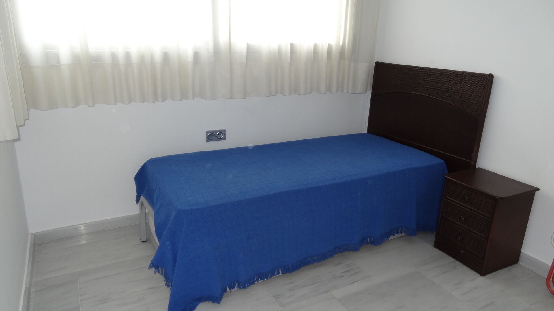 Una camera da letto con un letto singolo, un comodino e una finestra con tende leggere.