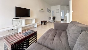 Ein modernes Wohnzimmer mit einem Flachbildfernseher, einem grauen Sofa und einem Vintage-Koffer.