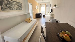 Ein modernes Wohnzimmer mit einer Couch, einem Esstisch mit Obst und einem Gemälde an der Wand.