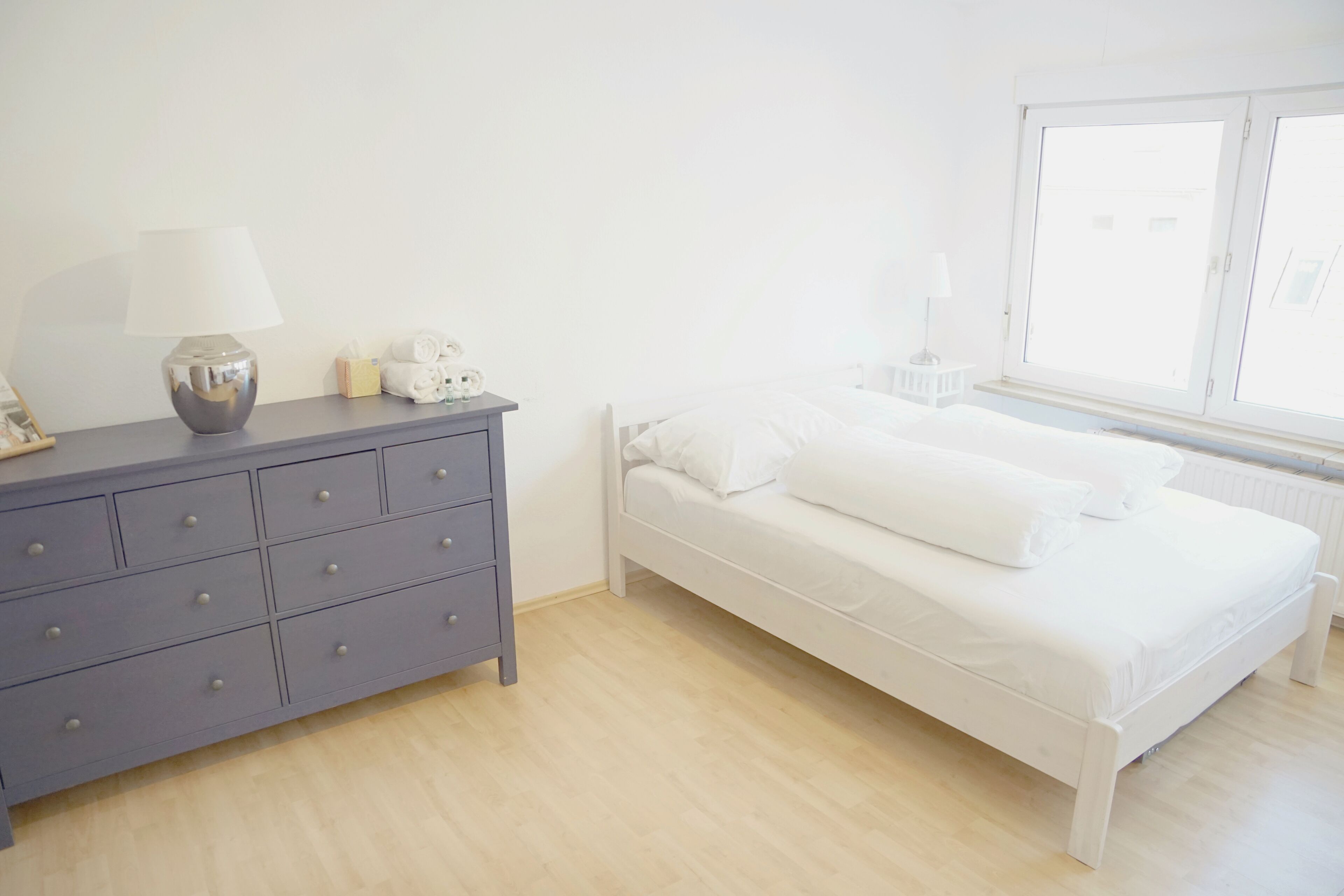 A bedroom with a bed, a dresser, a lamp, and a window.