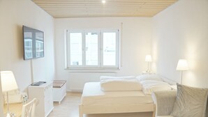 A modern, well-lit bedroom with a large window, a bed, a bedside table with a lamp, and a TV mounted on the wall. - F10 APARTMENT Ulm • Apartment in the heart of Ulm (Ulm)