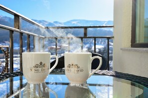 Two white cups with "King David Hotel" text on a glass table with a mountain view in the background. - King David Bakuriani (Borjomi)
