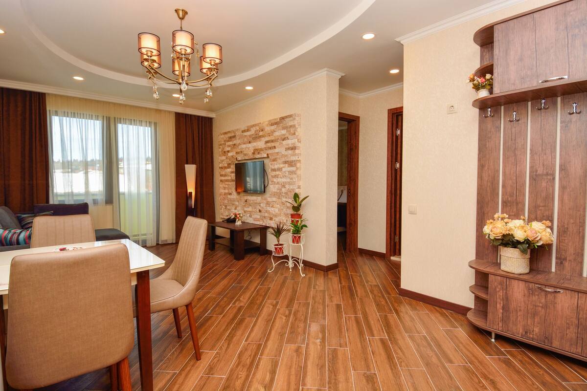 Un salon moderne comprenant un coin repas, un plancher en bois, un lustre et un mur d’accent en pierre.