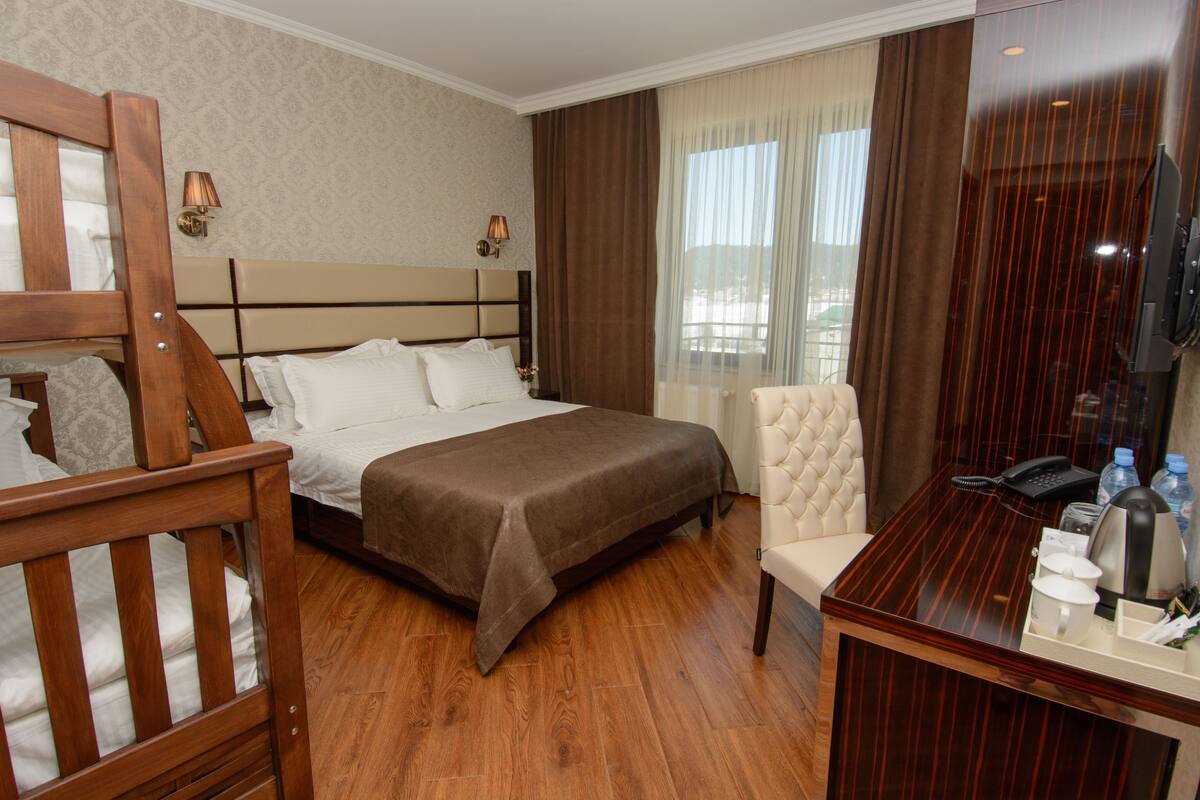 Une chambre d’hôtel avec un grand lit, une chaise en bois, un bureau avec un téléphone et des articles de toilette, ainsi qu’une télévision.