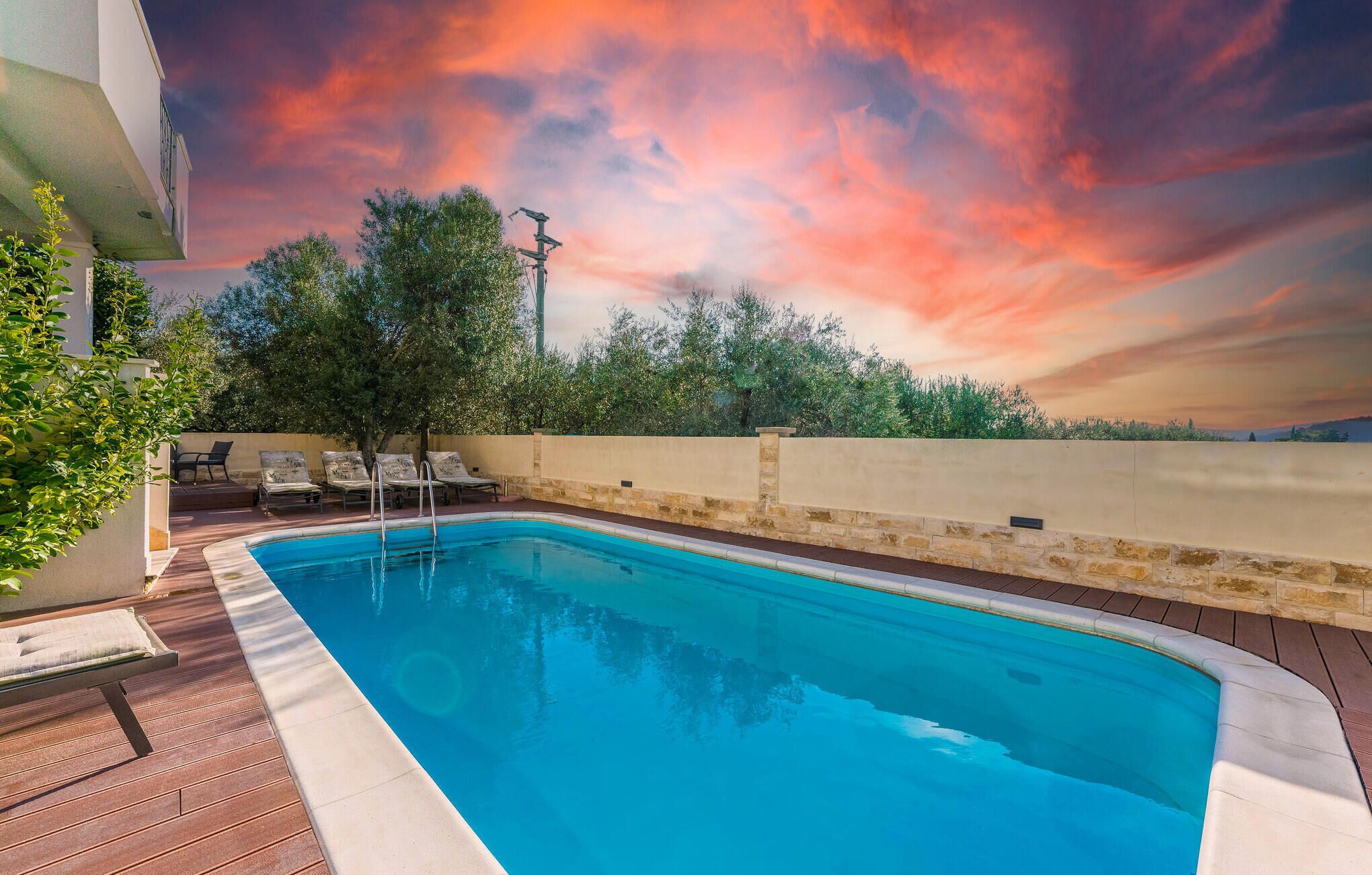 A swimming pool with lounge chairs and a sunset view.