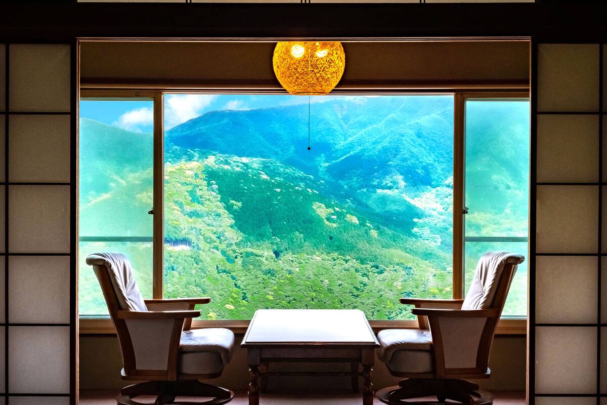 Une pièce dotée d’une grande fenêtre donnant sur un paysage montagneux. On y trouve une table et deux chaises.