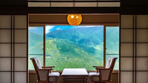 A room with a large window offering a view of a mountainous landscape. There is a table with two chairs and a hanging light fixture above. - Shirayu no Yado Yamadaya (Hakone)
