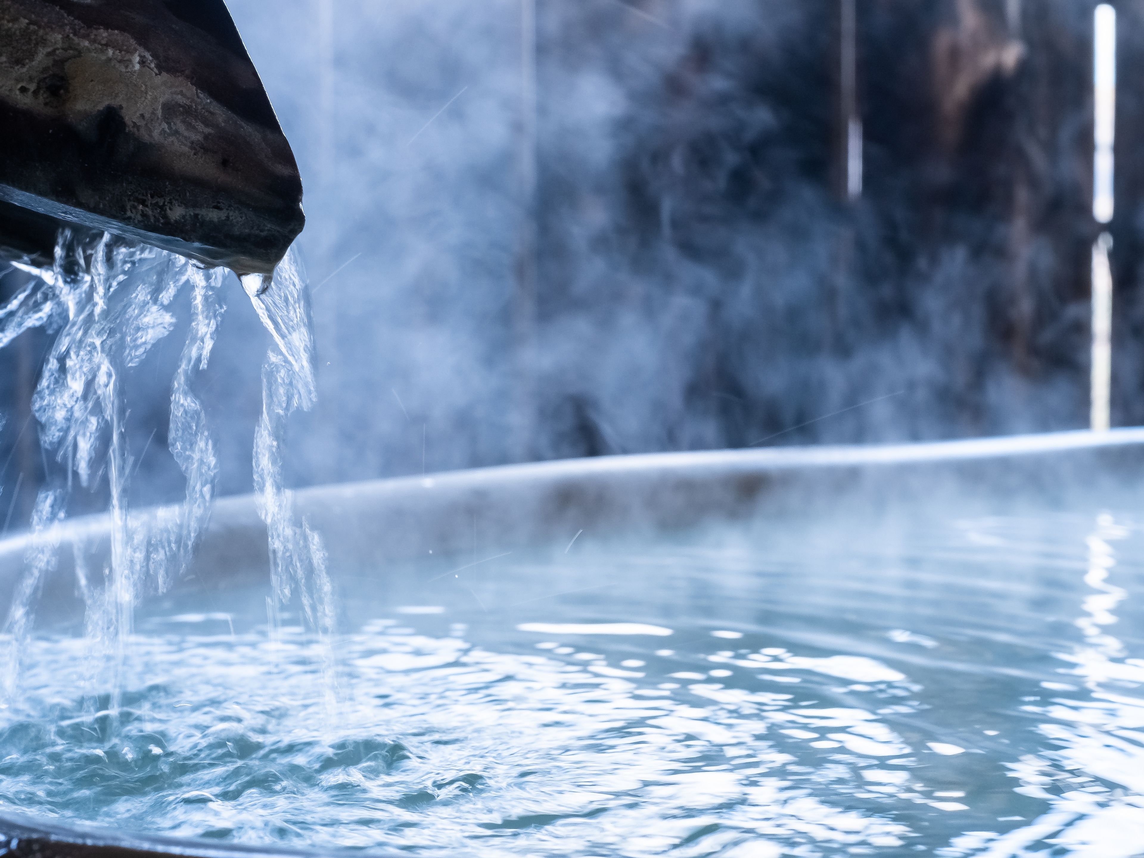 Primer plano de agua fluyendo de un caño hacia una piscina, rodeada de bruma.