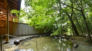 Ein traditionelles japanisches Onsen mit einer Holzdielen-Terrasse, einem Steingarten und umgebendem Wald.