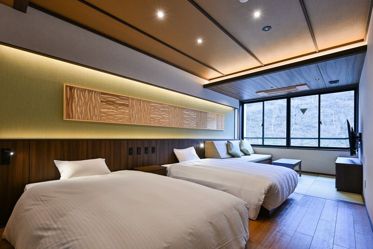 Une chambre d’hôtel moderne avec deux lits, une grande fenêtre et un plafond décoré avec du bois.