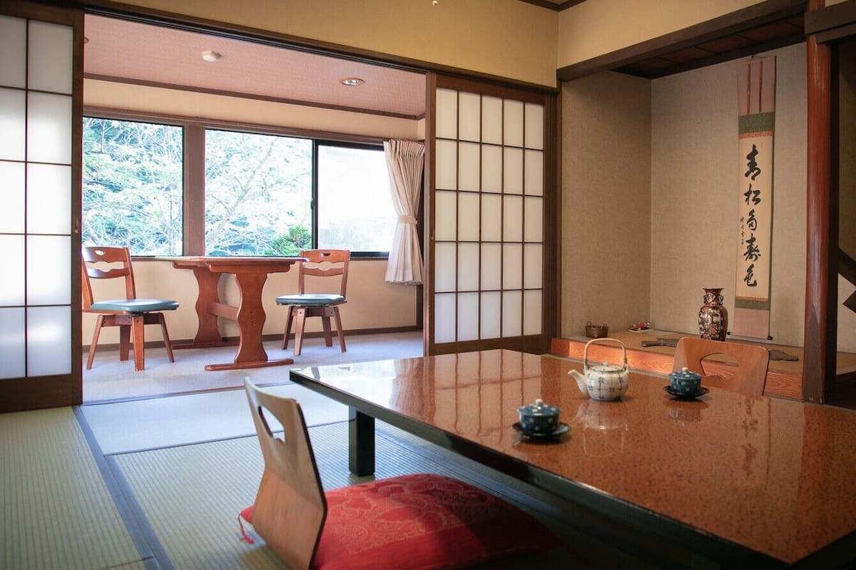 Una habitación japonesa tradicional con suelo de tatami, una mesa baja con sets de té y puertas correderas.