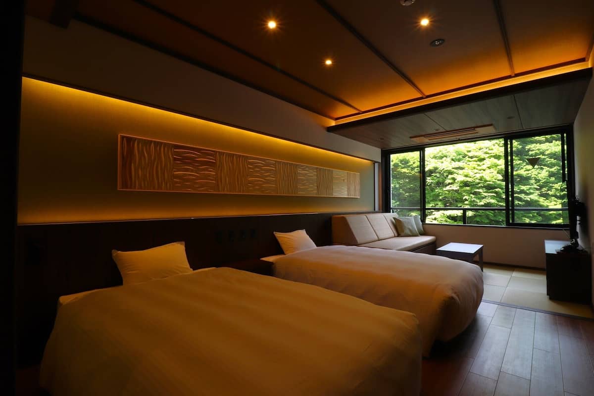 Habitación de hotel con dos camas, un ventanal con vistas a la vegetación y una obra de arte colgada en la pared.