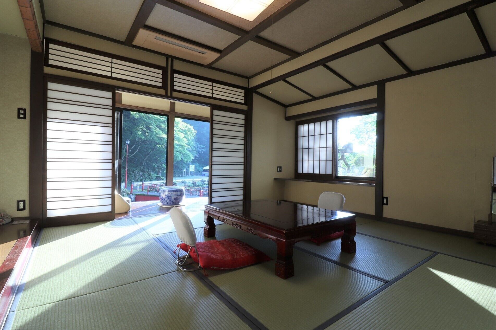 A traditional Japanese room with tatami flooring, a low wooden table, and sliding doors with a view of greenery outside.