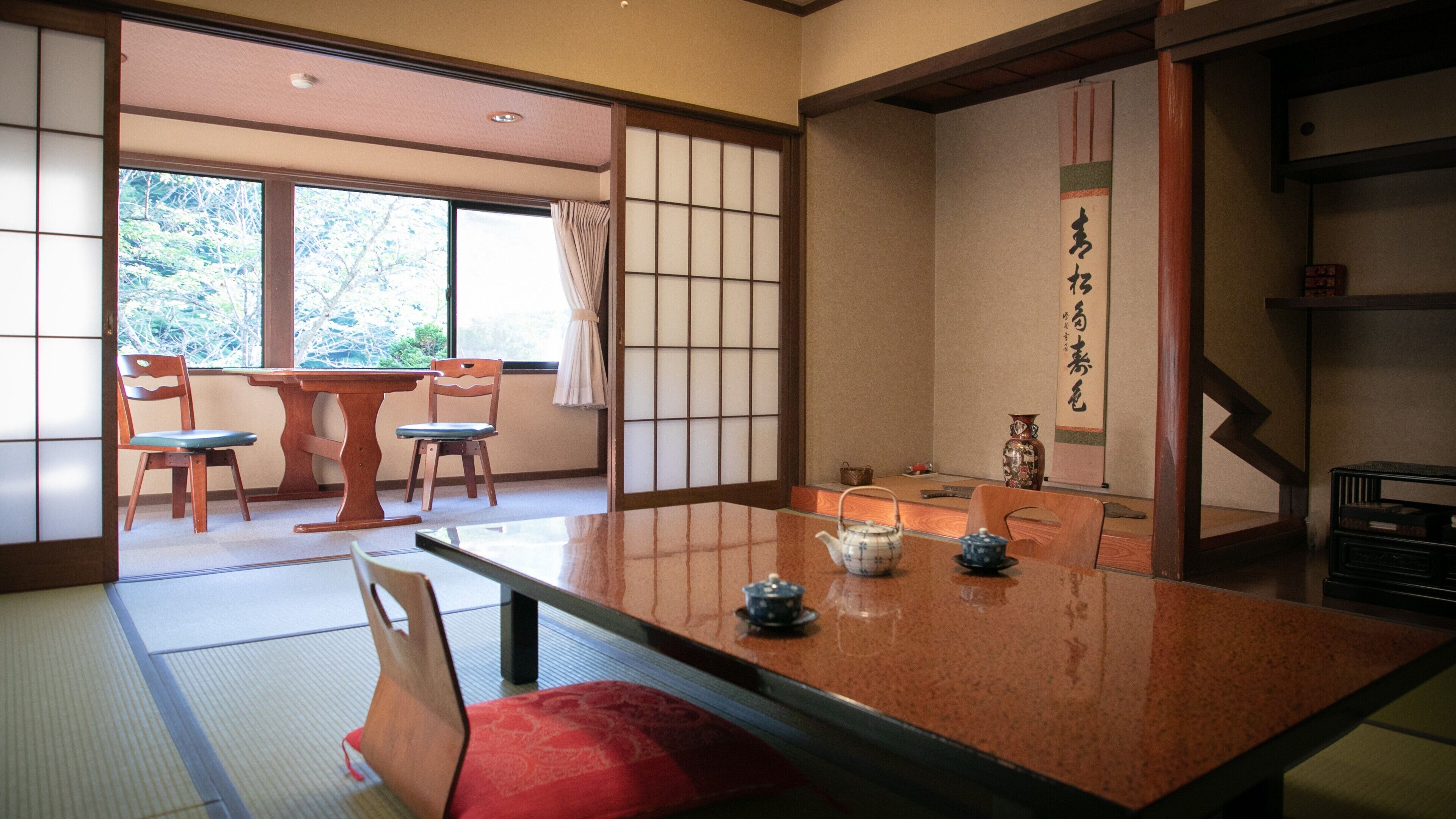 A traditional Japanese room with tatami flooring, a low table with tea set, sliding doors, and a view of trees outside.