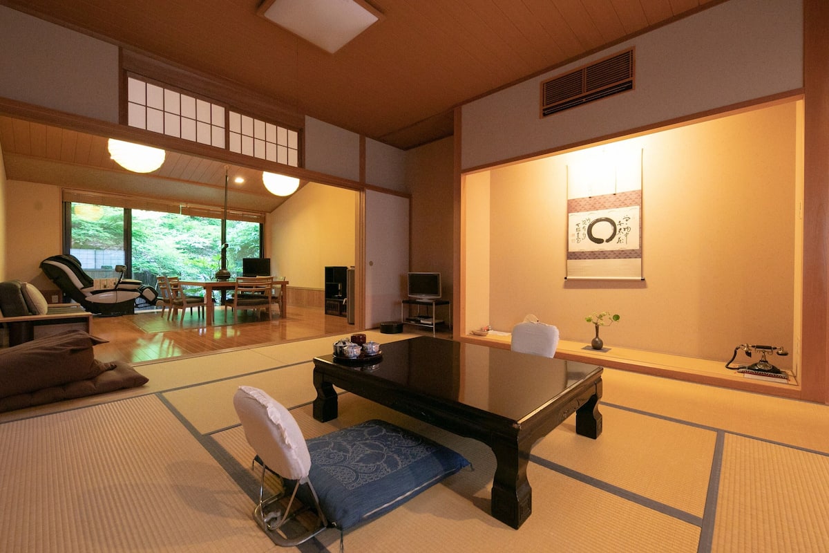 Una habitación tradicional japonesa con suelo de tatami, una mesa baja, un sofá y un televisor.