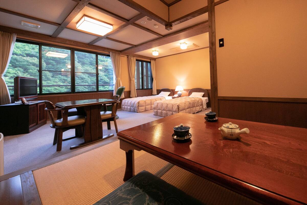 Una habitación de hotel con una mesa de comedor de madera, dos camas, un televisor y vistas a zonas verdes.