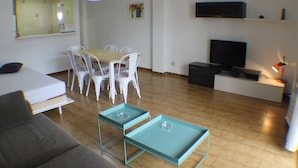 Una sala de estar moderna con sofá, mesa de comedor, sillas, televisor y un mueble bajo.