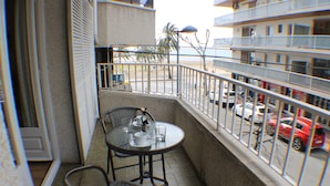 Un balcón con mesa y sillas, con vista a una calle con coches aparcados y una palmera.