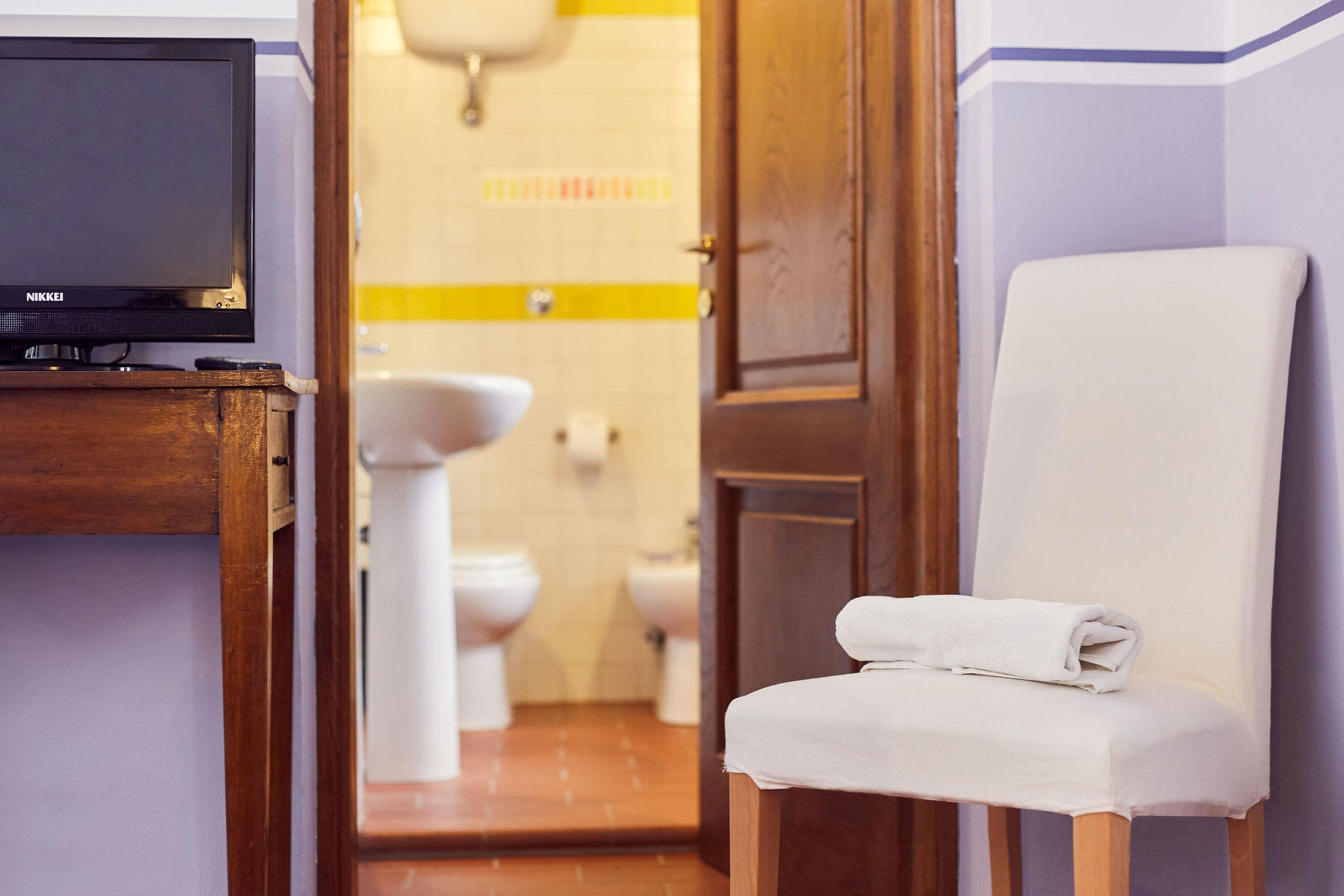 Un baño con un armario de madera, televisor, una silla blanca y un inodoro.