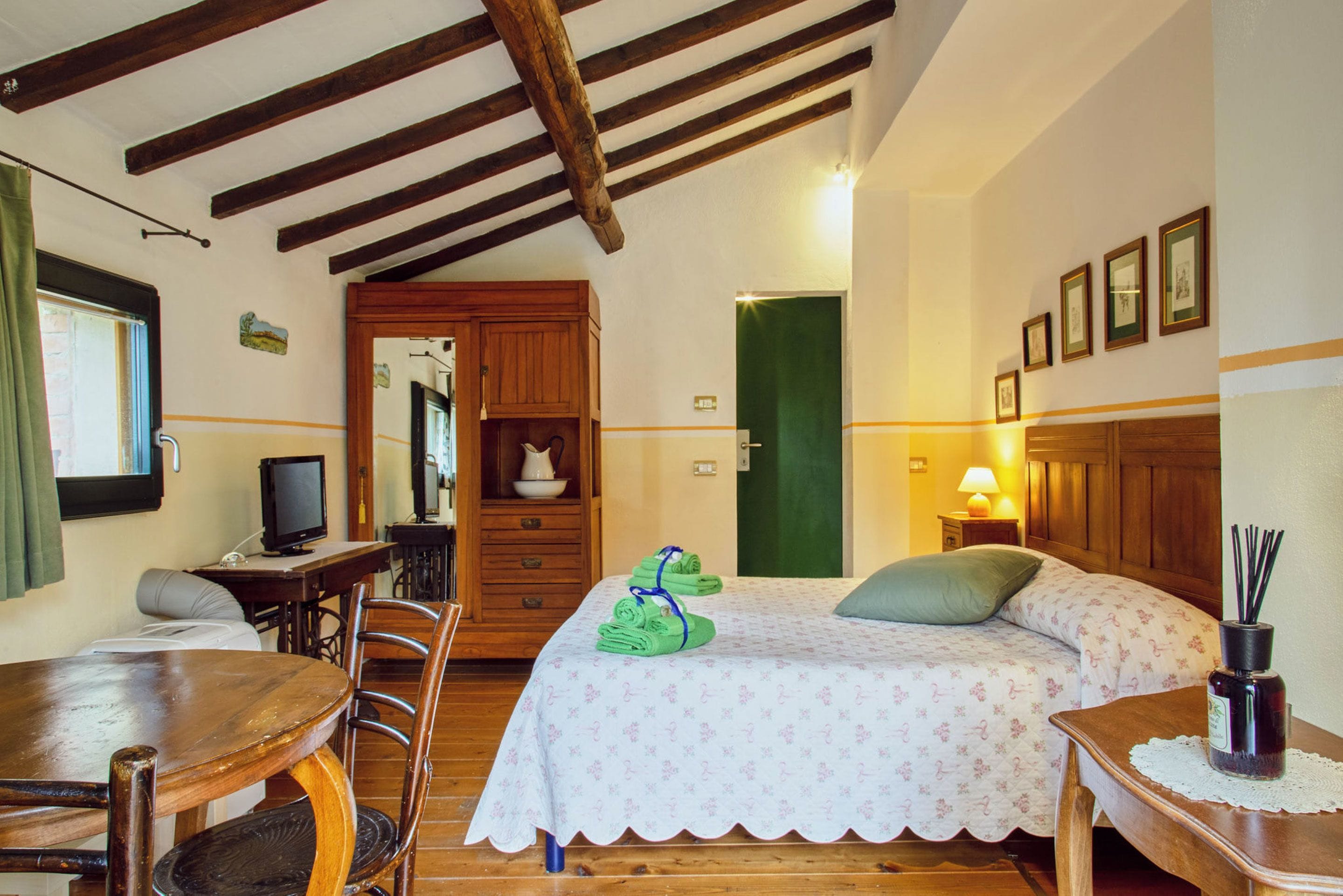 Une pièce confortable avec un lit, un bureau, une chaise, un téléviseur et un plafond en bois.