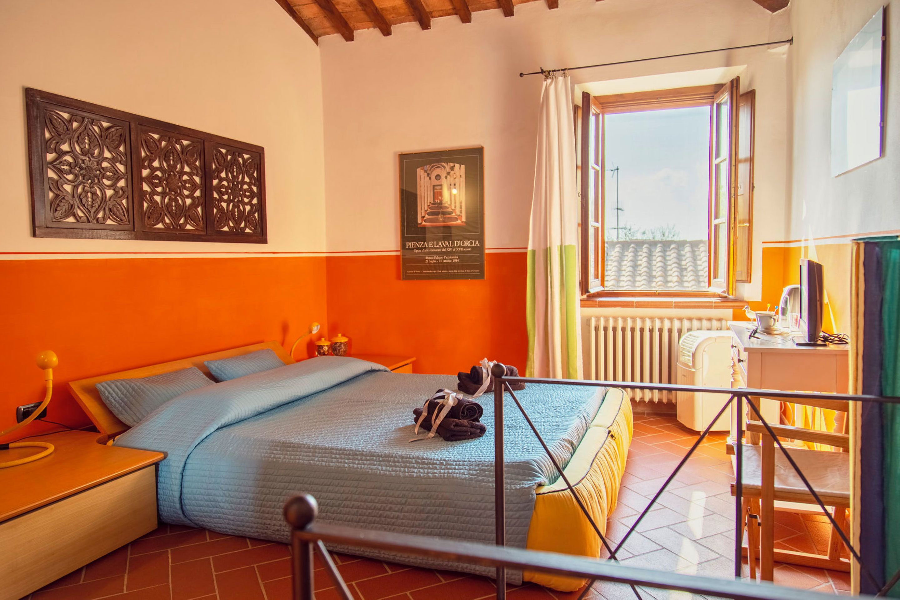 A bedroom with a bed, a nightstand, a window with curtains, and a radiator.