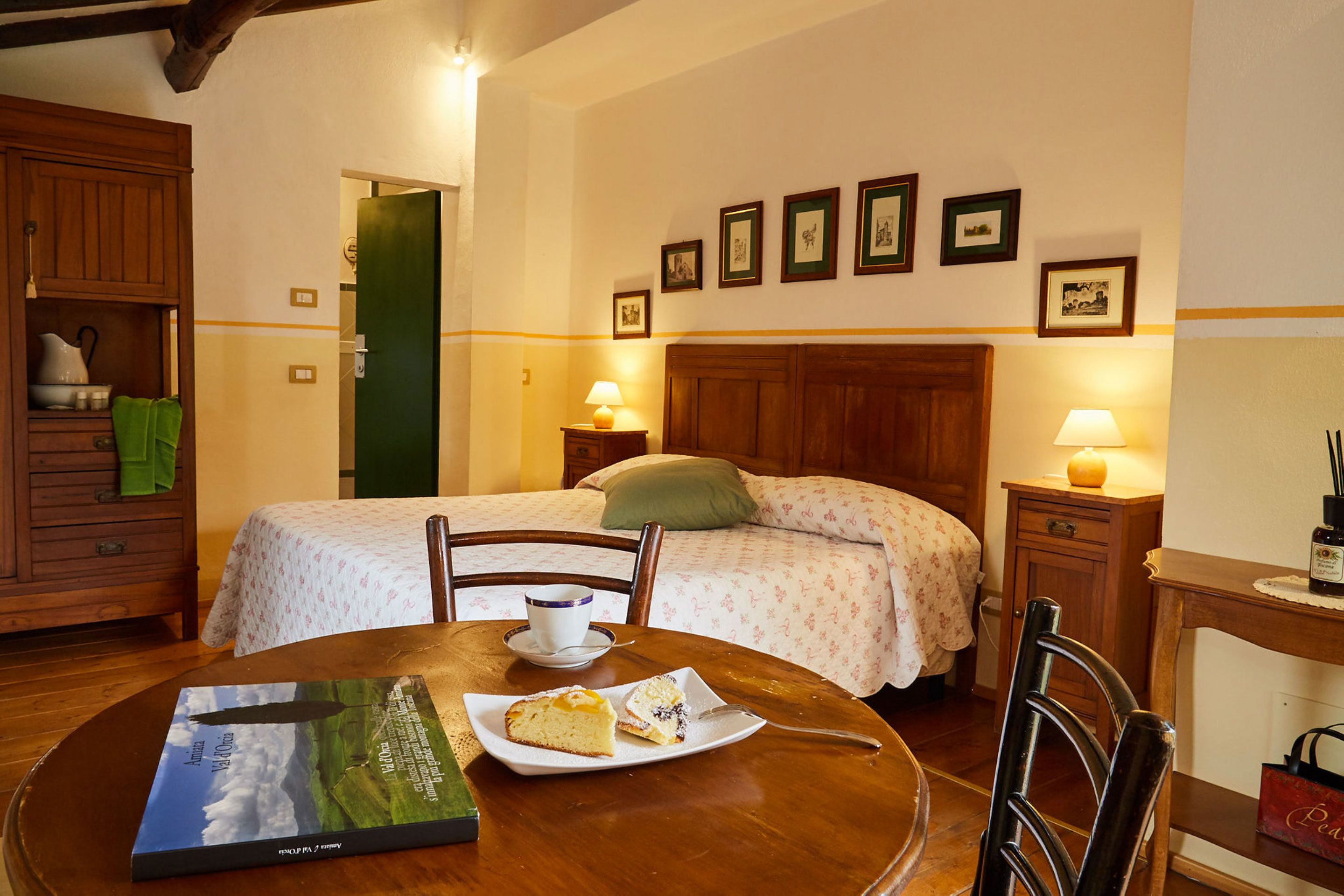 A neatly arranged hotel room with a bed, bedside tables, a dining table with a book and a plate of food, and a chair.